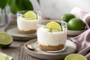 Limetten-Cheesecake im Glas ohne Backen ohne Gelatine – vier Portionsgläser mit cremiger Limettencreme auf Keksboden, garniert mit Limettenscheiben und Minze