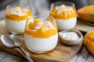 Mango-Kokos-Dessert im Glas: cremige Schichten aus Mangopüree und Kokoscreme, garniert mit Kokosraspeln und Limettenzeste