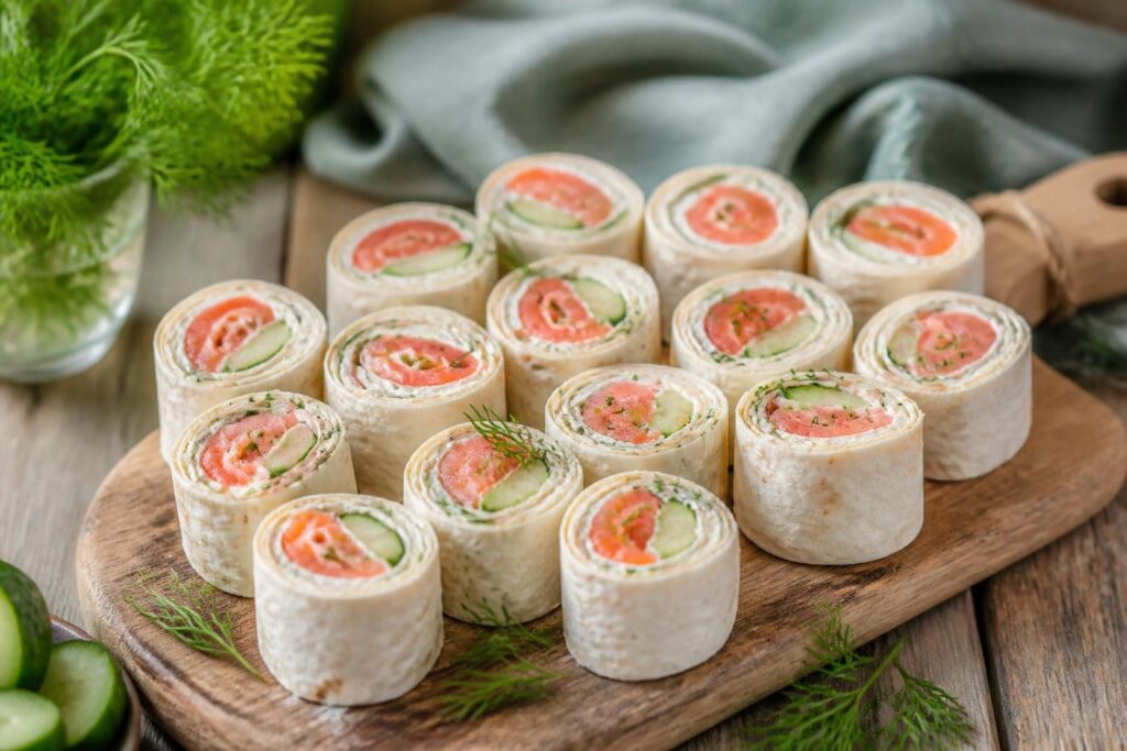 Wrap-Röllchen mit Räucherlachs und Gurke auf einem Holzbrett – schnelles Fingerfood für Buffet und Party