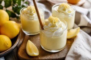 Zitronencreme im Glas ohne Ei, garniert mit frischen Beeren und Zitronenscheibe auf hellem Holzuntergrund