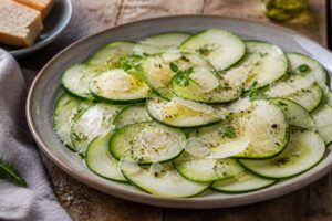 Zucchini-Carpaccio mit gehobeltem Parmesan, Pistazien und Zitronenmarinade auf einem weißen Teller, von oben fotografiert